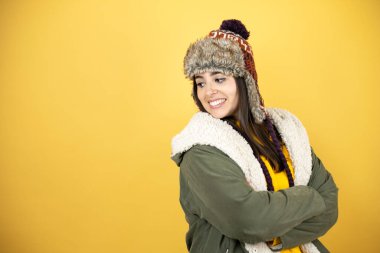 Sarı arka planda yeşil ceketli ve şapkalı güzel bir kadın kameraya gülümsüyor.