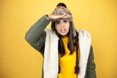 Sarı arka planda yeşil ceketli ve şapkalı güzel bir kadın çok mutlu ve tebessüm ediyor. arama kavramı.