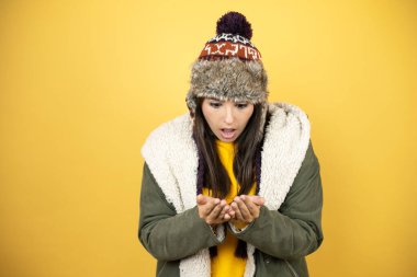 Sarı arka planda yeşil bir palto ve şapka giyen genç ve güzel bir kadın avuçlarını birbirine değdirirken ya da el hareketi yaparken gülümsüyor. Tutun ve koruyun