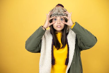 Sarı arka planda şapka ve yeşil kışlık ceket giyen güzel bir kadın gözlerini parmaklarıyla açmaya çalışıyor, uykulu ve yorgunluktan yorgun.