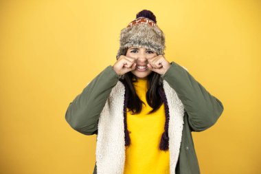 Sarı arka planda yeşil bir palto ve şapka giyen genç ve güzel bir kadın depresif ve endişeli, sinirli ve korkmuş. Üzücü ifade.