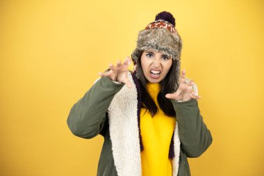 Sarı arka planda yeşil ceketli, şapkalı güzel bir kadın kedi gibi pençe hareketi yapıyor. Saldırgan ve seksi bir ifade.