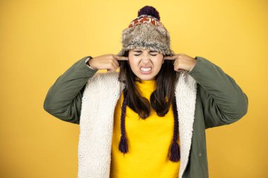 Sarı arka planda yeşil bir palto ve şapka giyen genç ve güzel bir kadın yüksek sesli müziğin sesi için rahatsız edici ifadeleri olan parmaklarıyla kulakları kapatıyor. Sağır kavramı.