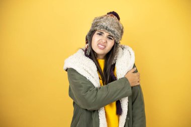 Genç, güzel bir kadın, sarı arka planda yeşil bir palto ve şapka giyiyor. Omzunda ağrı ve acı dolu bir ifade var.