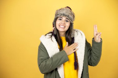 Sarı arka planda yeşil bir palto ve şapka giyen genç, güzel bir kadın gülümsüyor, yemin ediyor, yemin ediyor.