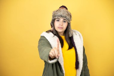 Sarı arka planda yeşil ceketli ve şapkalı güzel bir kadın bir numaralı parmaklarıyla işaret ediyor.