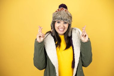 Sarı arka planda yeşil ceketli, şapkalı güzel bir kadın. Umut dolu bir gülümsemeyle işaret ediyor ve bakıyor.