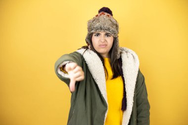 Sarı arka planda yeşil ceketli, şapkalı genç ve güzel bir kadın. Kızgın bir yüzü var.