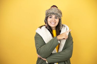 Sarı arka planda yeşil ceketli, şapkalı, güzel bir kadın gülümsüyor.