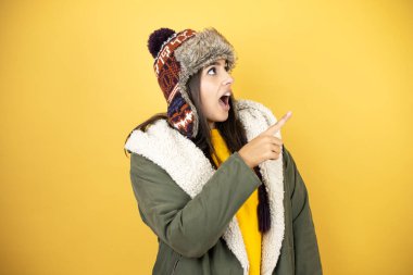 Sarı arka planda yeşil ceketli ve şapkalı güzel bir kadın el ve parmak uçlarını işaret ederek şaşırdı.