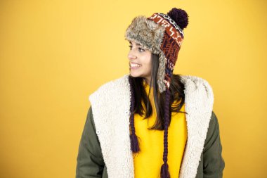 Sarı arka planda yeşil ceketli ve şapkalı güzel bir kadın yan tarafa gülümsüyor.