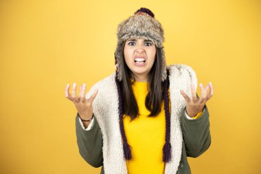 Sarı arka planda yeşil bir palto ve şapka giyen genç ve güzel bir kadın sinirli bir ifadeyle bağırıyor ve kollarını kaldırıyor. Hayal kırıklığı konsepti.