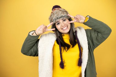 Sarı arka planda yeşil ceketli, şapkalı genç ve güzel bir kadın barış sembolü yapıyor. Yüzünde parmaklar, yüzünde neşeyle zafer işareti yapıyor.