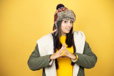 Sarı arka planda yeşil bir palto ve şapka giyen genç ve güzel bir kadın ellerini kavuşturup gülümseyerek gevşemiş ve neşeli bir şekilde dua ediyor. Başarı ve iyimser