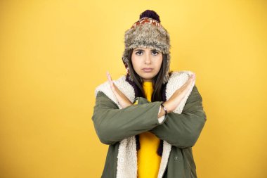 Sarı arka planda yeşil bir palto ve şapka giyen güzel bir kadın. Reddedilmiş yüz ifadesi. Kollarını kavuşturuyor.