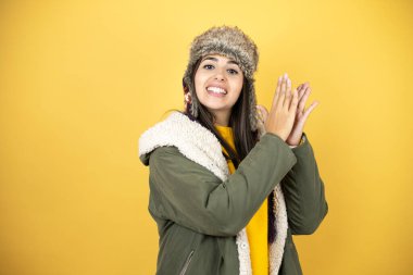 Sarı arka planda yeşil bir palto ve şapka takan genç güzel bir kadın alkışlıyor ve alkışlıyor. Mutlu ve neşeli, gururlu eller bir arada.