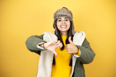 Sarı arka plan üzerinde yeşil bir palto ve şapka takan genç ve güzel bir kadın baş parmaklarını yukarı aşağı hareket ettiriyor, anlaşmazlık ve anlaşma ifadesi. Çılgın çatışma