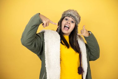 Sarı arka planda yeşil ceketli ve şapkalı güzel bir kadın bana elleriyle jest yapıyor.