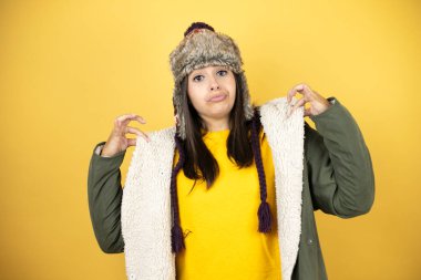 Sarı arka planda yeşil ceketli ve şapkalı güzel bir kadın tişörtünü başarıyla tutuyor.