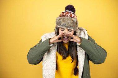 Sarı arka planda şapkası ve yeşil kışlık ceketi olan genç ve güzel bir kadın elleri ağızda bağırıyor ve bağırıyordu.