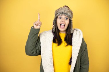 Sarı arka planda yeşil ceketli, şapkalı genç ve güzel bir kadın parmağını kafasında gezdirmiş ve bir fikri olduğunu düşünüyor..