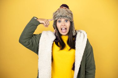 Sarı arka planda yeşil ceketli, şapkalı, güzel bir kadın gülümseyip parmaklarıyla kafasında bir fikri olduğunu düşünüyor..