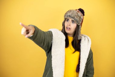 Sarı arka planda yeşil ceketli, şapkalı, genç ve güzel bir kadın. Parmakları önde, ağzı açık, şaşırmış, ön tarafta bir şey var.