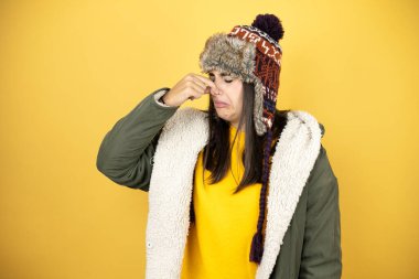 Sarı arka planda yeşil bir palto ve şapka giyen güzel bir kadın pis ve iğrenç bir koku alıyor. Dayanılmaz bir koku.