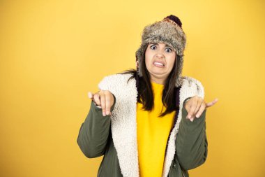 Sarı arka planda yeşil bir palto ve şapka giyen genç ve güzel bir kadın tiksinti dolu bir ifade takınıyor ve tiksinti tepkisi yüzünden tiksinti ve tiksinti ifadesi takınıyor. Sinir bozucu.