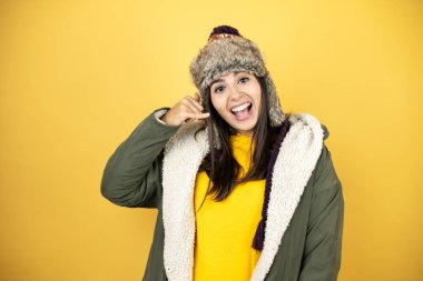 Sarı arka planda yeşil ceketli, şapkalı güzel bir kadın telefonda el ve parmaklarıyla gülümsüyor, telefonda konuşuyor gibi.