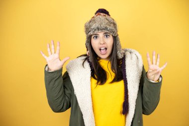 Sarı arka planda yeşil ceketli ve şapkalı güzel bir kadın dokuz numaralı parmaklarıyla gülümseyerek mutlu ve kendinden emin bir şekilde onu işaret ediyor.