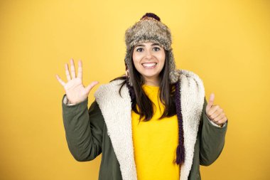 Sarı arka planda yeşil ceketli ve şapkalı güzel bir kadın altı numaralı parmaklarıyla gülümseyerek kendinden emin ve mutlu bir şekilde onu işaret ediyor.