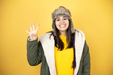 Sarı arka planda yeşil ceketli ve şapkalı güzel bir kadın dört numaralı parmaklarını gösterirken kendinden emin ve mutlu bir şekilde gülümsüyor.