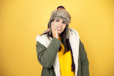 Sarı arka planda yeşil ceketli genç ve güzel bir kadın. Sarı saçlı, sarı arka planda duran güzel bir kadın. Diş ağrısı ya da diş ağrısı yüzünden ağız ve acı dolu bir ifadeyle birbirine dokunuyor.