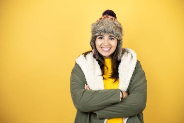 Sarı arka planda yeşil ceketli, şapkalı, güzel bir kadın. Güler yüzlü, kollarını kavuşturmuş dişlerini gösteren bir kadın.