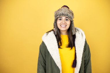 Sarı arka planda yeşil ceketli, şapkalı güzel bir kadın gülümsüyor