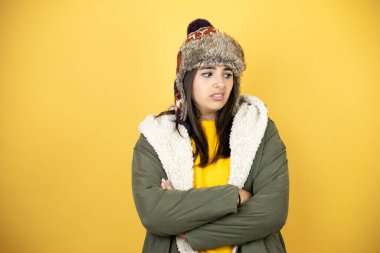 Sarı arka plan üzerinde yeşil bir palto ve şapka giyen genç ve güzel bir kadın çapraz kollardan sıkılmış ve yorgun görünüyor.