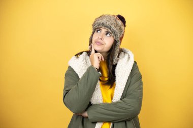 Sarı arka planda yeşil ceketli, şapkalı, güzel bir kadın. Düşünüp yan tarafa bakıyor.