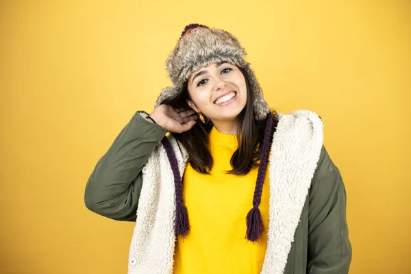 年轻美丽的女人头戴一顶帽子 身穿绿色冬衣 背景黄色 对着摄像机微笑 — 图库照片