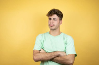Sarı arka planda yeşil tişört giyen yakışıklı adam çapraz kollardan sıkılmış ve yorgun görünüyor.