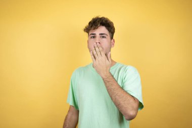 Sarı arka planda yeşil günlük tişört giyen yakışıklı adam ağzını eliyle kapatmasına şaşırdı.
