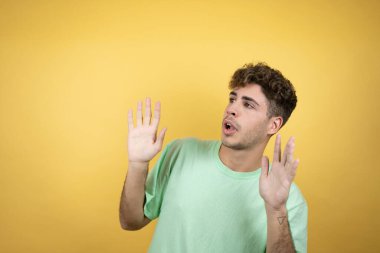 Sarı arka planda yeşil bir tişört giyen yakışıklı bir adam. Kolları yukarıdan düşmüş gibi korkmuş.