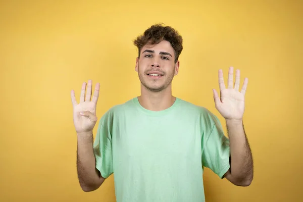 一个英俊的男人穿着一件黄色背景的绿色休闲衫 带着九号手指指尖 面带微笑 自信而快乐 — 图库照片