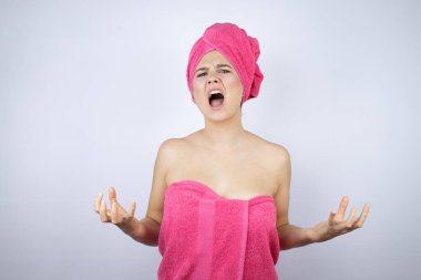 Genç, güzel bir kadın duş havlusu giyerek izole edilmiş beyaz arka planda duruyor deli gibi bağırıyor ve bağırıyor agresif bir ifade ve kollar havada. Hayal kırıklığı konsepti.
