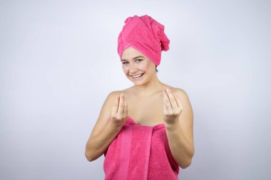 Banyodan sonra duş havlusu giyen genç bir kadın izole edilmiş beyaz arka planda duruyor. Elleriyle para hareketi yapıyor. Maaş ödemesi istiyor.