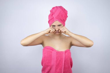 İzole edilmiş beyaz arka plan üzerinde duran duş havlusu giyen genç ve güzel bir kadın depresif, sinirli ve korkmuş bir şekilde ağlıyor. Üzücü ifade.