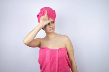 Genç, güzel bir kadın duş havlusu takıyor. İzole edilmiş beyaz arka planda duruyor. Alnında parmakları olan insanlarla dalga geçiyor..