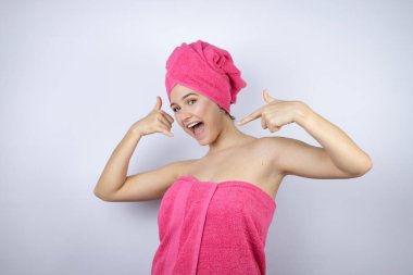 Banyodan sonra duş havlusu giyen genç ve güzel bir kadın izole edilmiş beyaz arka planda duruyor. Bana elleriyle jest yapıyor.