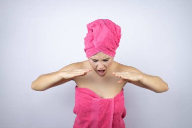 Genç, güzel bir kadın duş havlusu takıyor. İzole edilmiş beyaz arka planda duruyor. Elleri ağızda bağırıyor ve bağırıyor.