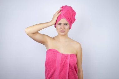 Banyodan sonra duş havlusu takan genç ve güzel bir kadın izole edilmiş beyaz arka planda duruyor. Bir elini başının üstüne koyup sanki bir şey unutmuş gibi gülümsüyor.